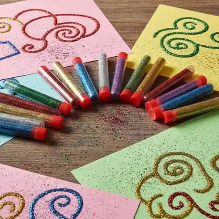 tubes filled with glitter on a wood table and paper crafts that have glitter around them