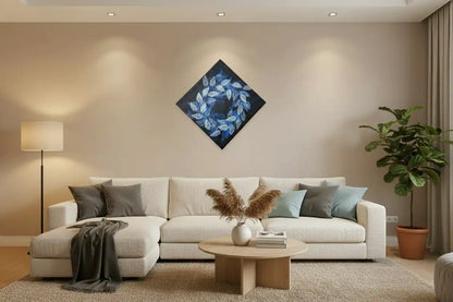 A modern living room featuring a diamond-shaped canvas wall art print with a blue leaf wreath design, hung above a white sectional sofa with neutral-toned pillows and a round wooden coffee table.