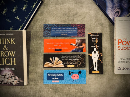 A set of laminated card-stock bookmarks with various designs, including text and illustrations, placed on a surface with books in the background.