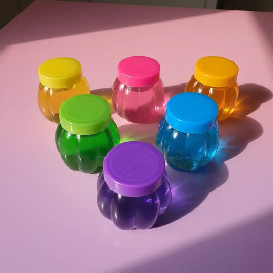Set of colorful transparent jars with lids on a pink surface