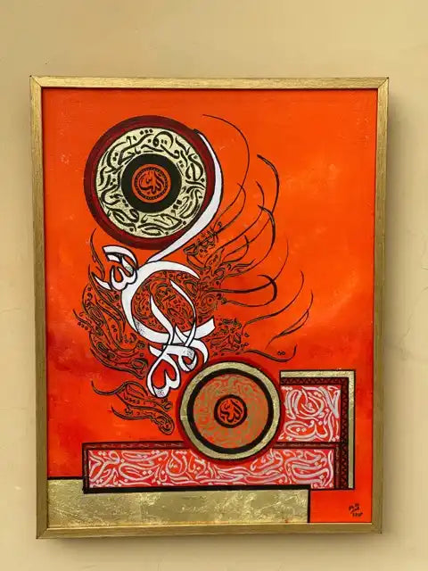 An abstract Arabic calligraphy painting in a gold frame, featuring vibrant orange, red, white, and black elements on a beige wall.