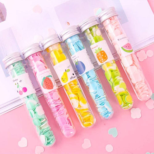Set of colorful test tube-shaped containers with fruit-themed designs on a pink background.