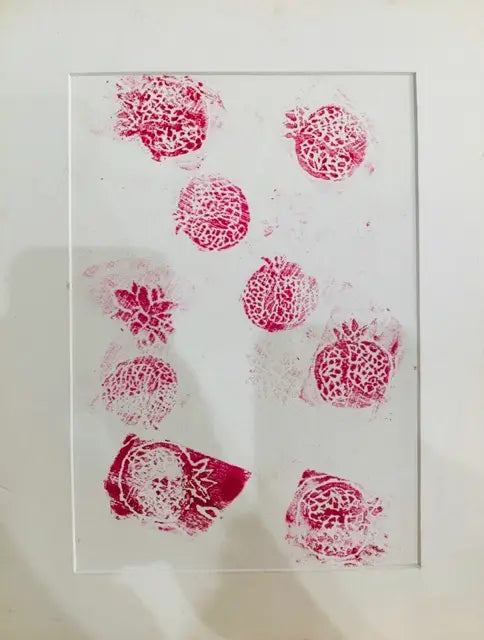A square white art print or card featuring multiple pink mottled fruit and leaf stamps, presented in a clear acrylic frame against a white background.
