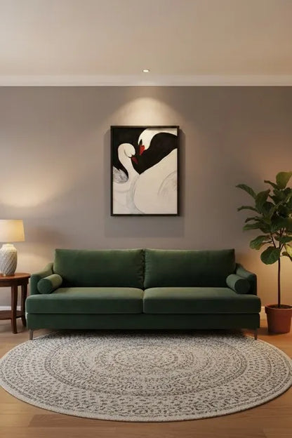 A modern living room setup featuring a dark green velvet sofa, a round patterned area rug, a potted fiddle-leaf fig plant, and a framed swan painting on a warm gray wall.