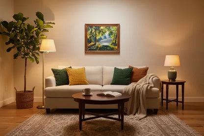 A cozy living room scene with a cream sofa, patterned green and yellow pillows, a round wooden coffee table, a floor lamp, and a framed landscape painting on the wall above the couch.