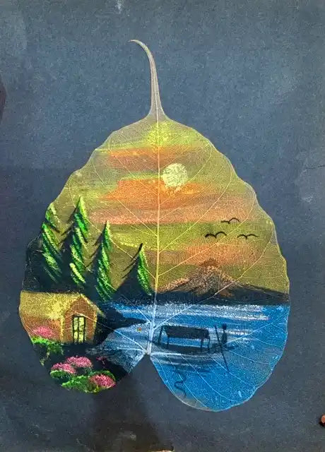 A leaf-shaped artwork or plaque featuring a painted landscape scene with a sunset sky, trees, water, a small cabin, flowers, and a boat, displayed against a dark background.