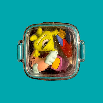 Colorful toy erasers inside a transparent container with blue handles on a teal background
