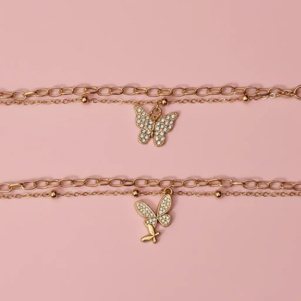 Two gold butterfly necklaces on a pink background