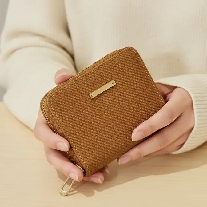 Brown textured wallet held by a person wearing a beige sweater on a beige surface