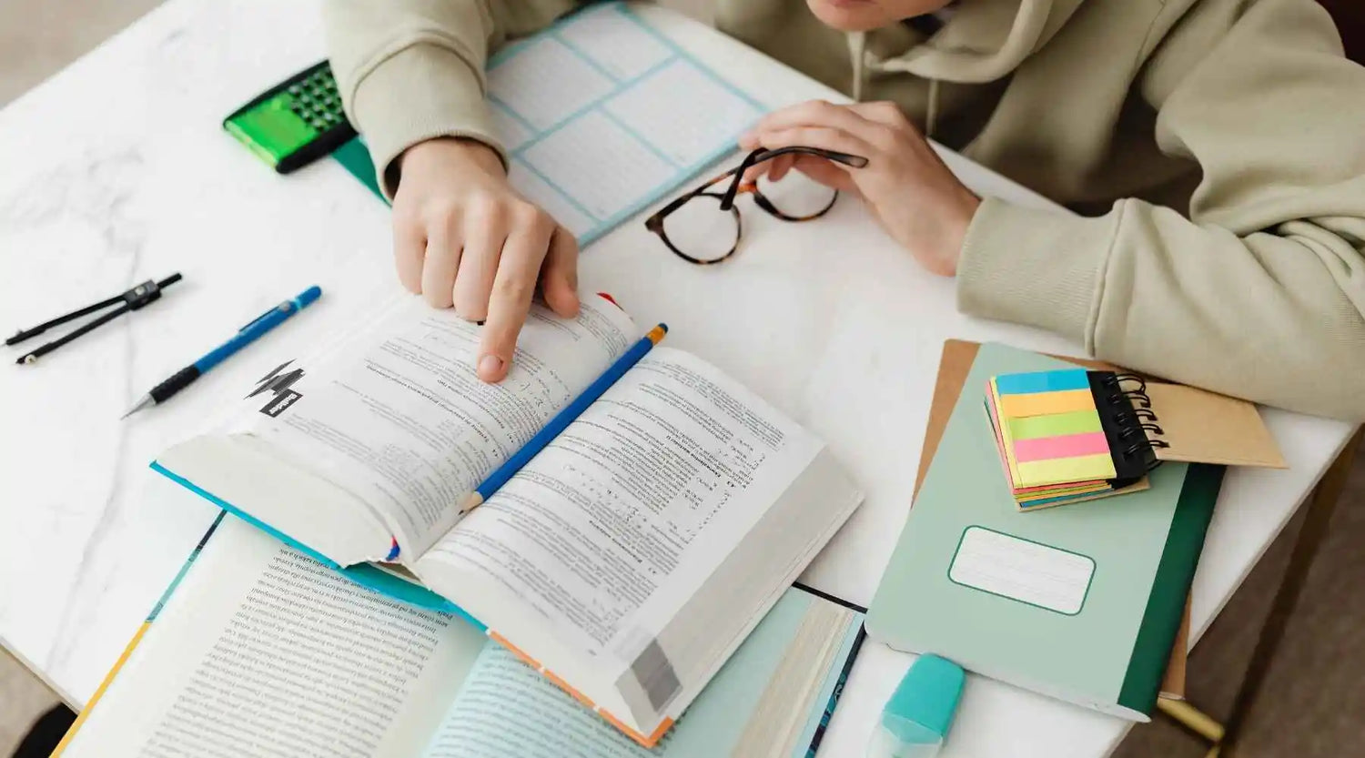 Person studying with books, notes, and stationery on a table
