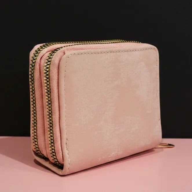 Pink wallet with gold zipper on a pink surface and black background