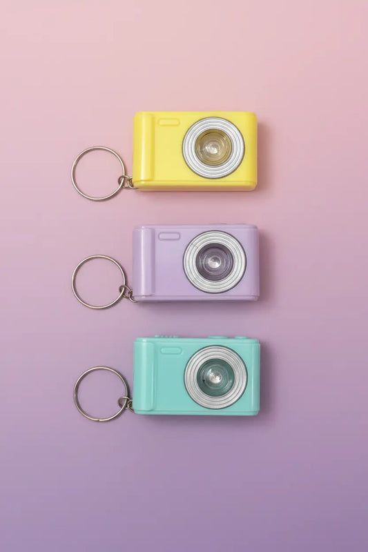 small cameras with lens and keychains on a light pink purple gradient background