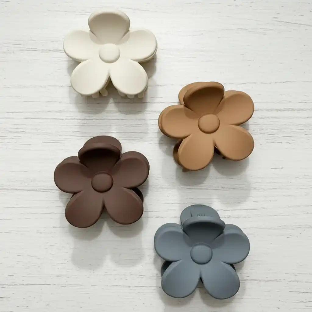 Four flower-shaped clips in white, brown, gray, and beige on a light wooden surface.