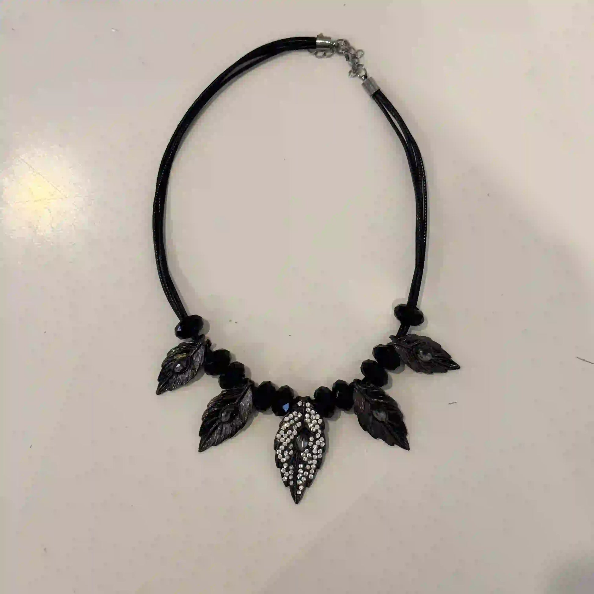 Black leaf-shaped necklace on a light gray background