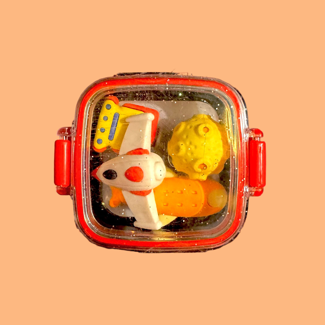 Colorful toy set in a transparent container with red lid on a peach background