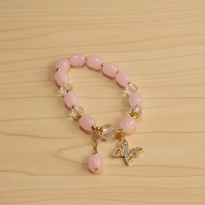 Pink beaded bracelet with butterfly charm on a wooden surface