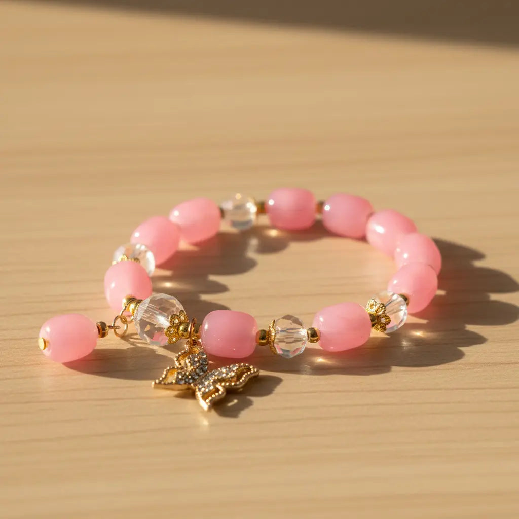 Pink beaded bracelet with a gold butterfly charm on a wooden surface