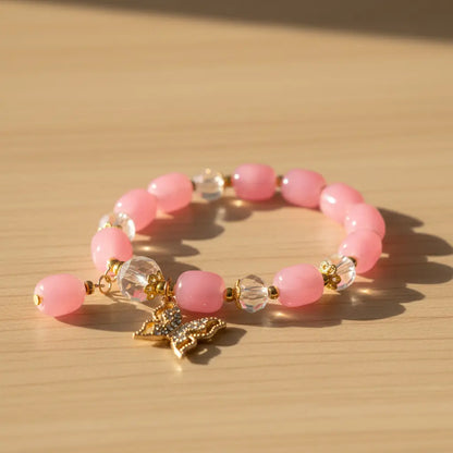 Pink beaded bracelet with a gold butterfly charm on a wooden surface