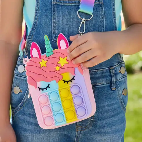 Child holding a colorful unicorn-themed pop-it bag with a blurred outdoor background