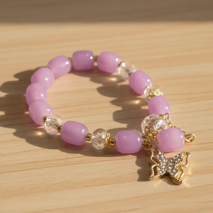 Pink beaded bracelet with a gold butterfly charm on a wooden surface