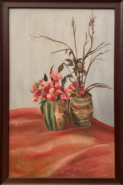 A framed still life painting featuring pink flowers in two textured vases on a draped red-orange surface against a light gray background, enclosed in a dark brown wooden frame.