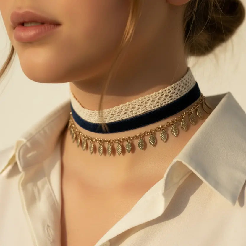 Close-up of a person wearing a gold necklace with leaf pendants, white lace choker, and beige shirt.