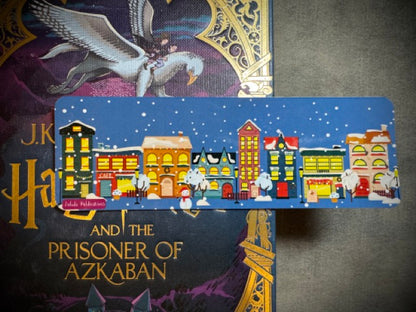 A winter themed laminated card stock bookmark depicting images of a winter town placed on a surface with a book.